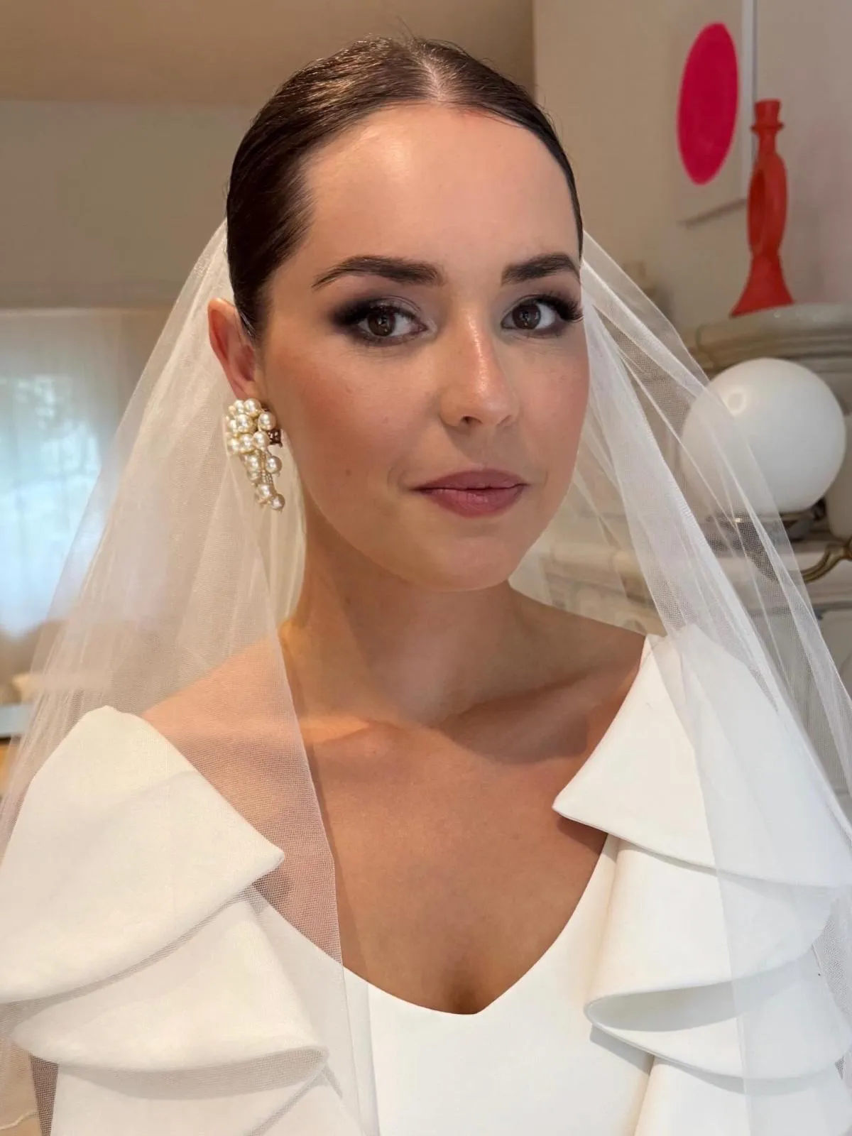 Nahaufnahme einer Braut mit Schleier und Perlenohrringen, sanftem Smokey Eye und makellosem Teint.
