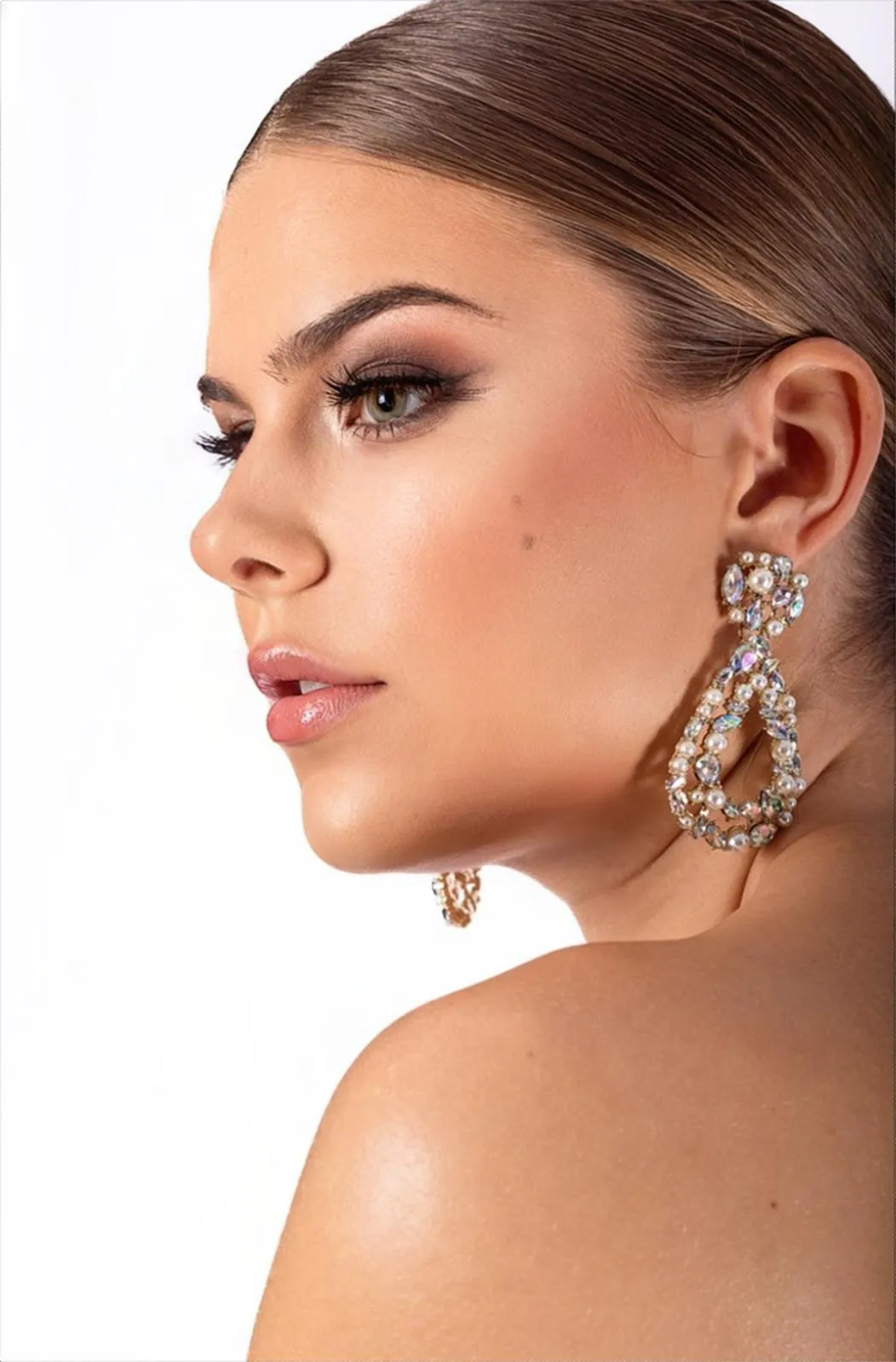 Nahaufnahme eines eleganten Beauty-Looks im Profil — sanfter Smokey Eye, makelloser Teint und funkelnde Perlen-Ohrringe.