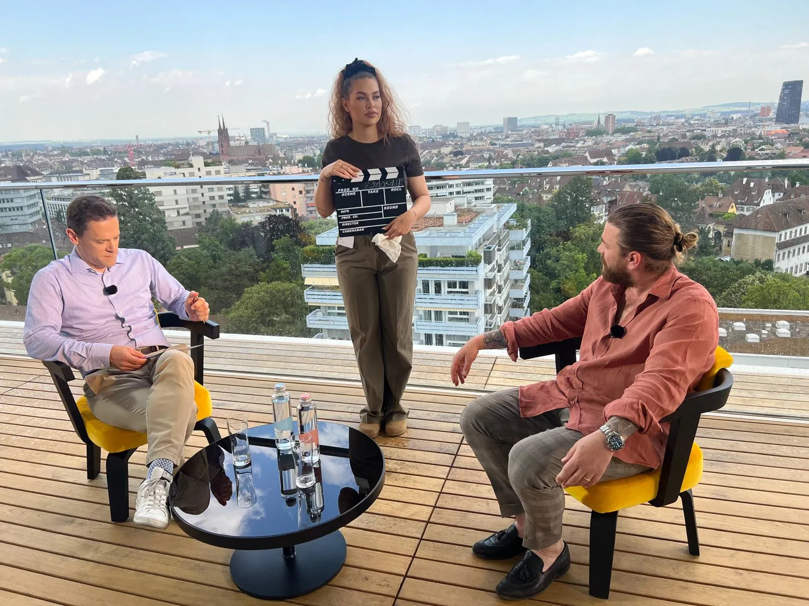 Sandra hält die Filmklappe während einer TV-Produktion auf einer Dachterrasse mit Blick über Basel.